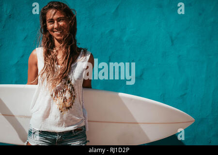 Heureux Surfer Girl with surfboard en face du mur bleu Banque D'Images