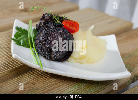 Morcilla (boudin frit avec du riz) servi sur plaque blanche avec purée de pommes de terre, tomates et herbes aromatiques Banque D'Images