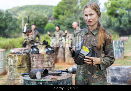 Portrait d'upset Girl standing avec le casque de protection avec une touche de peinture après coup direct au jeu de paintball Banque D'Images