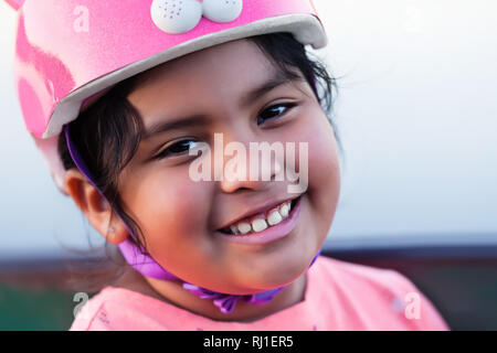 Smiling pre teen kid pluriethniques, avec un ensemble complet des dents et le port d'un casque de vélo rose. Banque D'Images