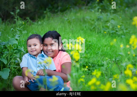 Un petit frère d'être tenu par sa grande sœur, assis ensemble dans un champ vert au printemps. Banque D'Images