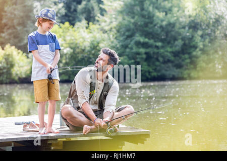 Smiling père à fils au comité permanent sur la jetée pendant que la pêche dans le lac Banque D'Images