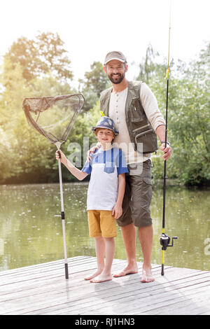 Full Length portrait of smiling père et fils debout avec matériels de pêche sur la jetée contre lake Banque D'Images
