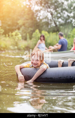 Portrait of smiling boy avec anneau gonflable flottant contre la navigation de plaisance au Lac Banque D'Images