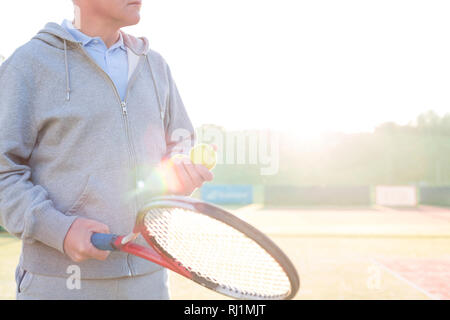 Portrait of mature man holding tennis racket sur cour contre un ciel clair Banque D'Images