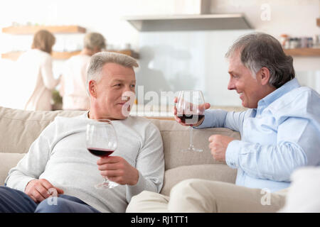 Smiling mature men holding wineglasses tout en parlant dans la salle de séjour à la maison Banque D'Images