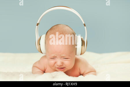 Beau bébé nouveau-né dans de grands écouteurs pour écouter de la musique, isolé sur fond bleu Banque D'Images