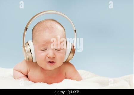 Beau bébé nouveau-né dans de grands écouteurs pour écouter de la musique, isolé sur fond bleu Banque D'Images