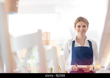 Portrait of smiling young waitress standing avec bloc-notes de restaurant Banque D'Images