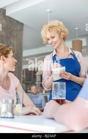 Smiling waitress à partir de la jeune femme assise, l'homme en restaurant Banque D'Images