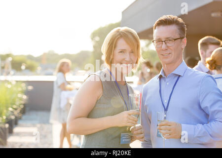 Portrait of smiling mature woman standing with wineglasses at party sur le toit Banque D'Images