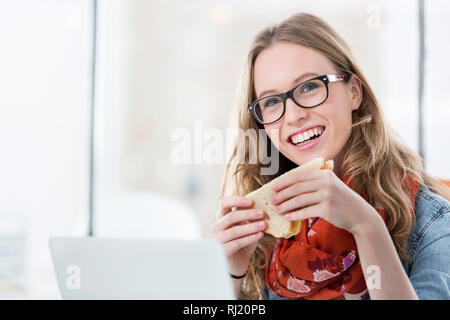 Portrait of happy businesswoman holding sandwich dans office Banque D'Images