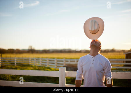 Agriculteur souriant son chapeau sur son nez tout en se tenant près d'une clôture sur sa ferme au soleil. Banque D'Images