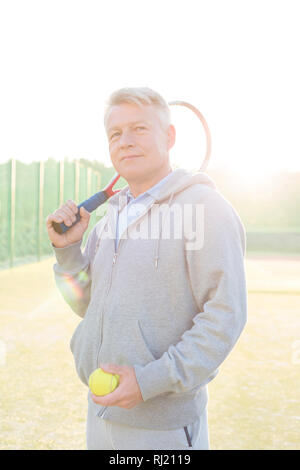 Retour allumé d'homme confiant holding tennis ball et racket sur cour contre un ciel clair Banque D'Images