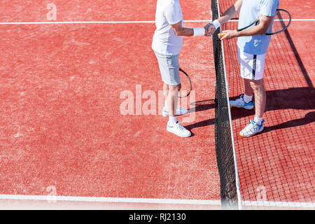 La section basse des hommes se serrer la main en se tenant debout par tennis net sur cour rouge au cours de match Banque D'Images