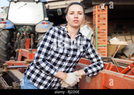 Young woman propriétaire de ferme moderne posant près de tracteur Banque D'Images