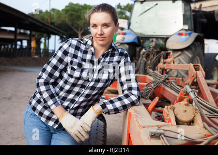 Young woman propriétaire de ferme moderne posant près de tracteur Banque D'Images