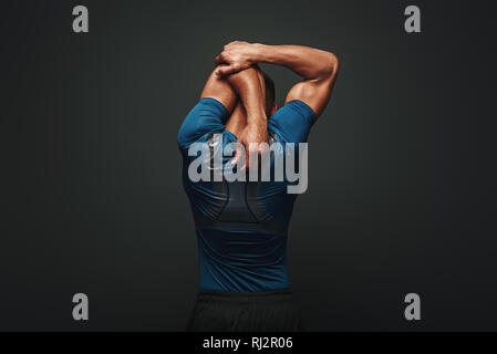 Portrait de jeune homme fort musclé s'étendant ses bras. African Male fitness model debout sur fond sombre. Vue arrière Banque D'Images