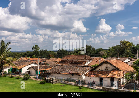 Belavadi, Karnataka, Inde - 2 novembre, 2013 : le toit en tuiles rouges du petit village sous ciel bleu avec des nuages blancs. Bande de végétation verte sep Banque D'Images