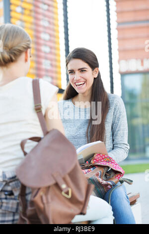 Smiling teenage girl sitting avec un ami sur un banc à l'université campus Banque D'Images