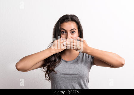 Belle Jeune femme debout dans un studio en studio, couvrant la bouche avec les mains. Banque D'Images