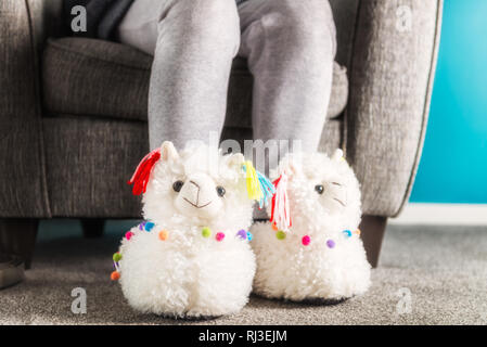 Jeune fille porte 3d soft mignon chaussons de lama, lors de la lecture sur le fauteuil gris Banque D'Images