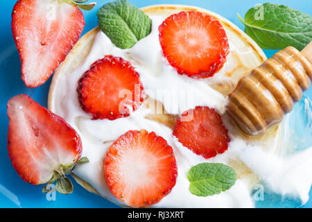 Crêpes aux fraises, miel et menthe sur une surface bleue Banque D'Images