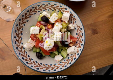 Ingrédients de salade grecque y compris les tomates, concombres, olives noires et fromage feta sont prêtes à manger dans un bol de céramique colorée sur table en bois Banque D'Images