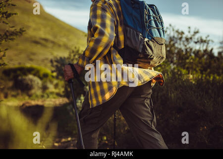 Trekking homme une colline holding les bâtons de trekking. Cropped Vue de côté d'un homme marchant sur une colline portant sac à dos. Banque D'Images