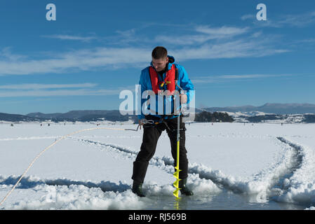 Young Caucasian man drilling la glace sur un lac gelé avec glace jaune percer la vis sans fin portant des gilets. Selective focus Banque D'Images