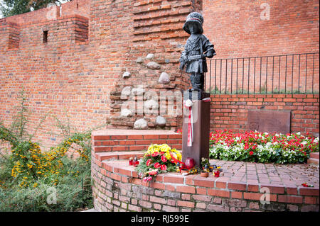 Petit garçon d'insurgés memorial à Varsovie, Maly powstaniec Antek décoré de rouge blanc ruban Polonais, des fleurs et des bougies votives, mur de briques rouges beh Banque D'Images