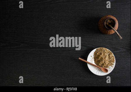 Photographie artistique de la yerba mate infusion, typique de l'Argentine, dans une assiette blanche, sur un fond de bois foncé Banque D'Images