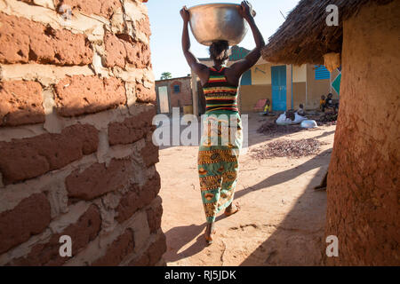 Village de Bodadigou, Banfora, région des Cascades, Burkina Faso, 4 décembre 2016; une femme retournant à son composé transportant un conteneur d'eau sur sa tête. Banque D'Images