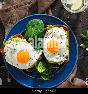 Vue de dessus les toasts avocat sain pour le petit déjeuner ou le déjeuner avec le pain de seigle, pain grillé et purée d'avocat d'œufs au plat sur table en bois sombre. Petit-déjeuner sain tabl Banque D'Images