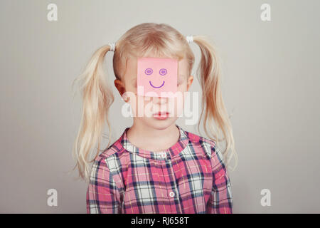 Closeup portrait of triste malheureux white Caucasian blonde preschool girl avec drôle sticky note sur son visage. Kid : exprimer des sentiments. Concept de di Banque D'Images