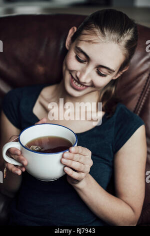 Junge Frau sitzt dans Sessel und trinkt Tee Banque D'Images