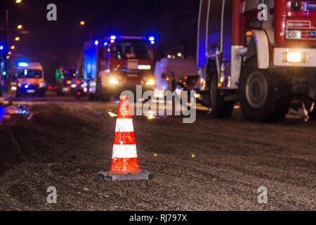 Un cône sur la route au cours de l'extinction d'incendie en hiver dans la soirée sur l'arrière-plan de camions incendie et ambulances Banque D'Images