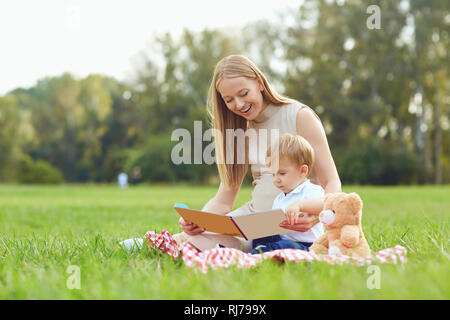 Mère avec enfant lit sur l'herbe dans le parc. Banque D'Images