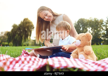 Mère avec enfant lit sur l'herbe dans le parc. Banque D'Images