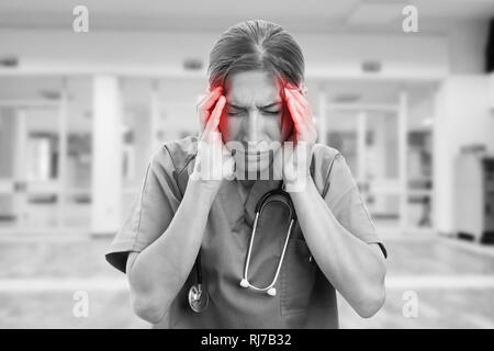 Photo noir et blanc d'infirmière avec maux de tête se tenant la main sur les temples de couleur rouge en tant que concept de la douleur Banque D'Images