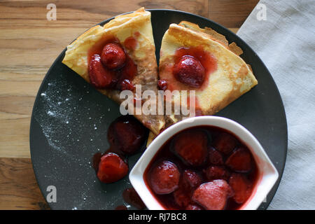 Crêpes maison avec du fromage cottage et les fraises dans une assiette. Fond de bois. Banque D'Images