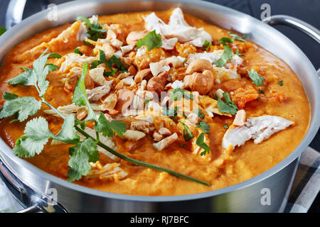 Close-up de soupe Mulligatawny épicé copieux avec de la viande de poulet frit arrosé avec dans un chaudron de cajou sur une table en bois noir, Indien et anglais c Banque D'Images