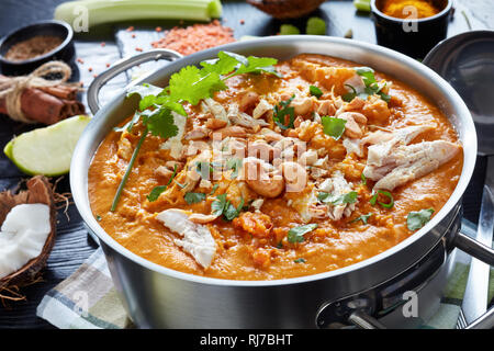 Soupe Mulligatawny épicé copieux avec de la viande de poulet frit arrosé avec dans un chaudron de cajou sur une table en bois noir avec des ingrédients, Affaires indiennes et l'engl Banque D'Images