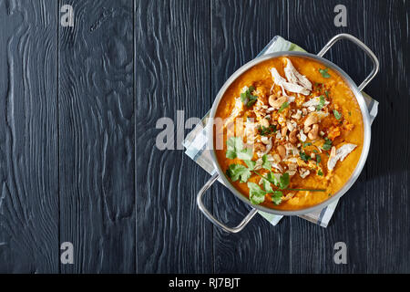 Soupe Mulligatawny épicé chaleureux avec la viande de poulet et le lait de coco saupoudré de cajou frits dans un chaudron sur une table en bois noir, Indien et engl Banque D'Images