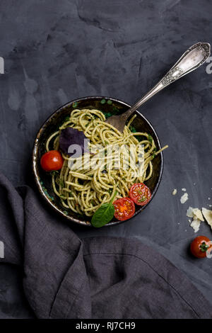 Pâtes au pesto dans un bol avec une fourchette au fond sombre. Le fromage, les tomates cerises et près de serviette. Concept de cuisine italienne. Vue d'en haut Banque D'Images