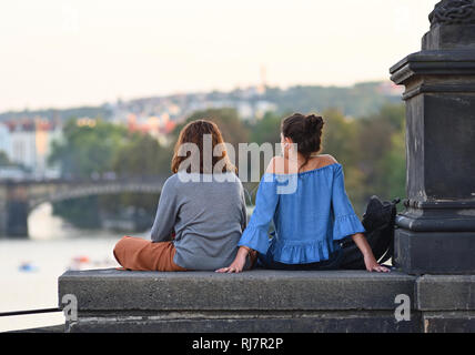 Deux jeunes filles assis sur le pont Charles à Prague, République tchèque, à écouter la musique et profiter de soir vue sur la Vltava. Banque D'Images