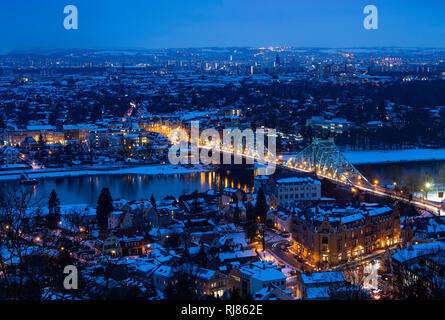 Dpatop - 05 février 2019, Saxe, Dresde : Les toits des maisons sont couvertes de neige à l'heure bleue. Les voitures roulent sur le pont éclairé Blaues Wunder (photo avec une longue exposition) sur le côté droit de la photo. Photo : Monika Skolimowska/dpa-Zentralbild/dpa Banque D'Images