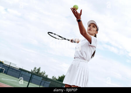 Jolie femme en blanc sportswear avec la raquette et la balle dans ses mains est prêt à frapper la balle sur la cour Banque D'Images