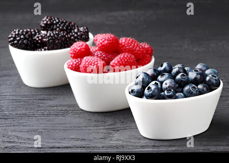 Bleuets frais, framboises et mûres dans un bol blanc sur fond de bois noir, selective focus Banque D'Images