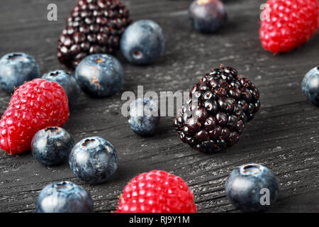 Bleuets frais, framboises et mûres sur fond de bois noir, selective focus. Banque D'Images